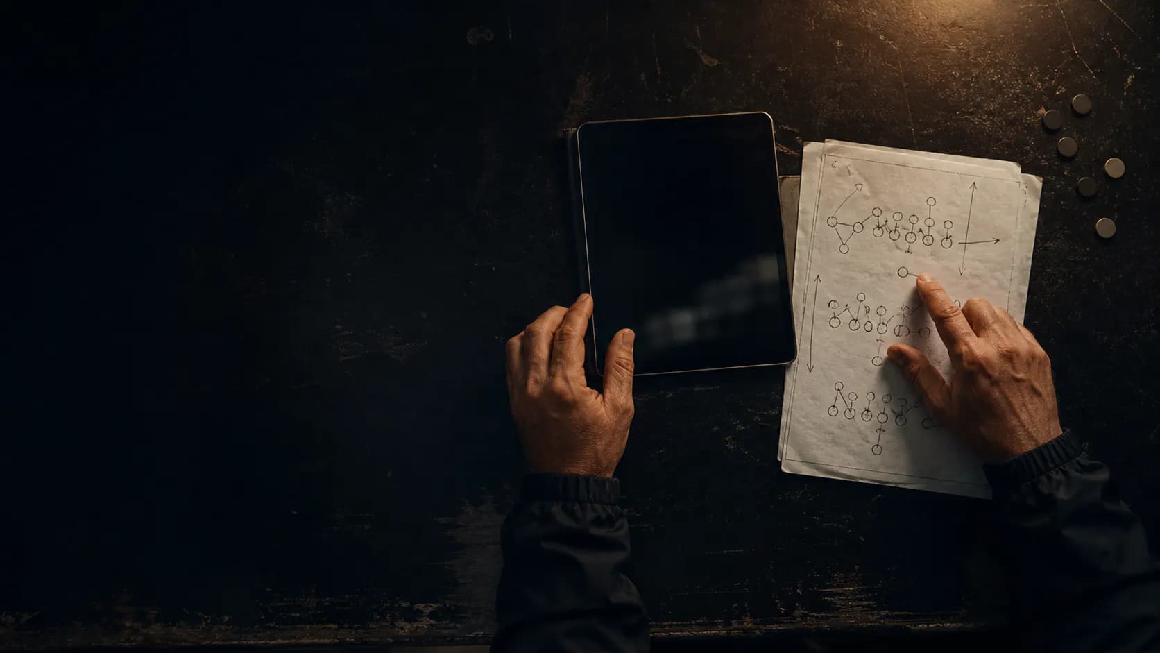A coach reviewing a football play sheet beside a tablet